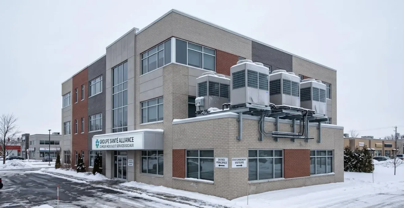 Immeuble commercial de bureaux du Grand Montréal en hiver avec neige au sol, ciel gris québécois et unités extérieures de thermopompes commerciales visibles sur la façade latérale